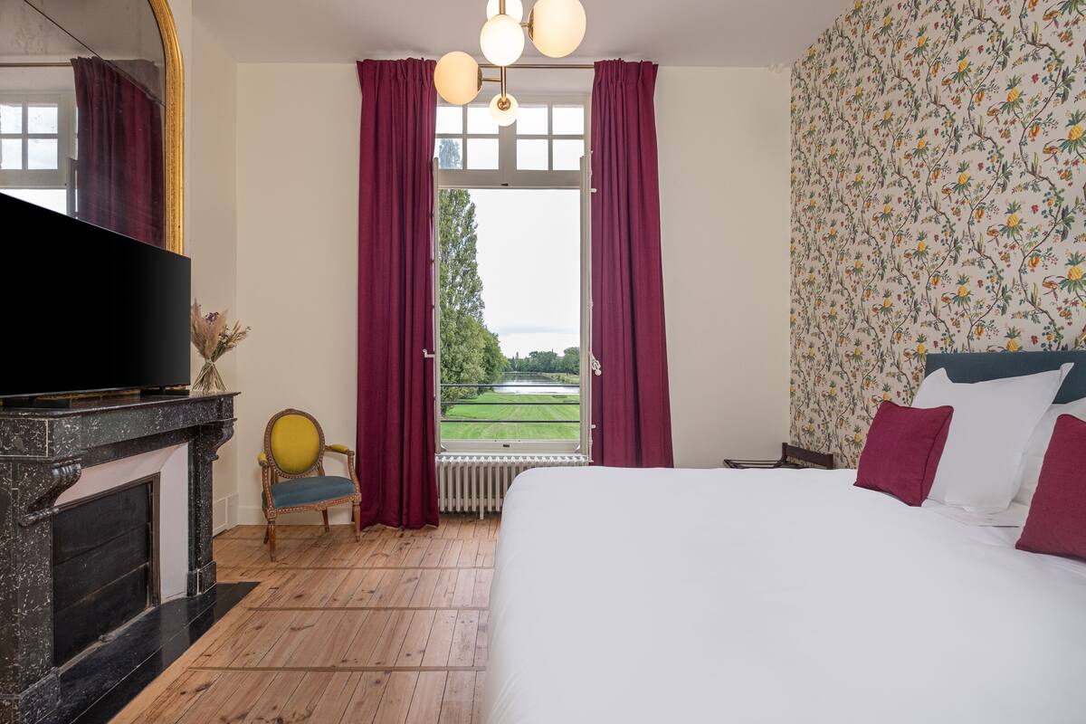 Een slaapkamer met een bed, een televisie, een open haard en uitzicht op een tuin.