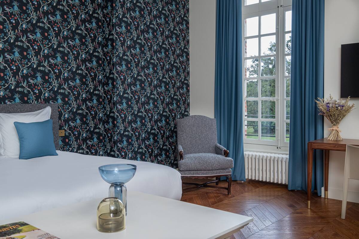Een hotelkamer met een bed, een stoel, een tafel en een raam met gordijnen.