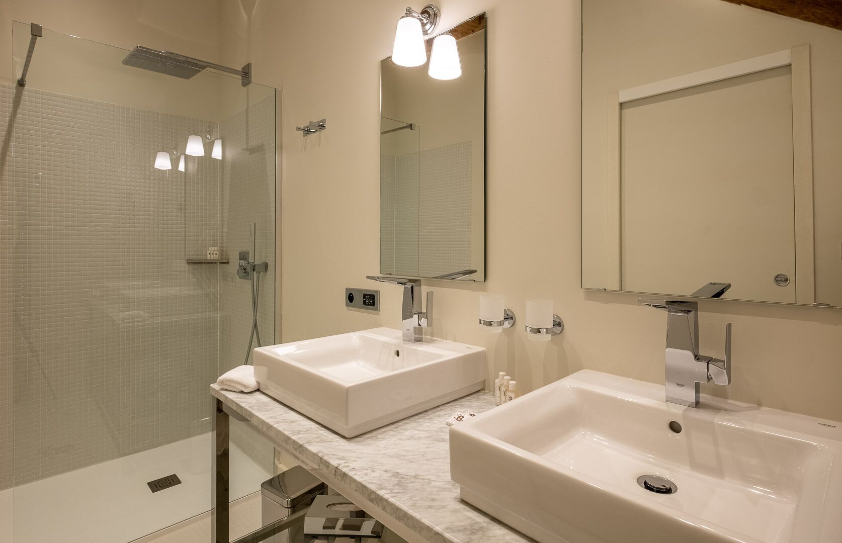 A modern bathroom with two sinks, a glass shower enclosure, and a large mirror.