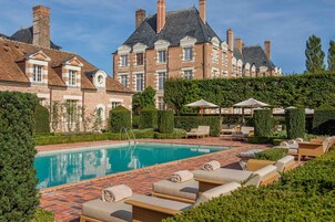 Área de piscina com espreguiçadeiras e um edifício de tijolos ao fundo.