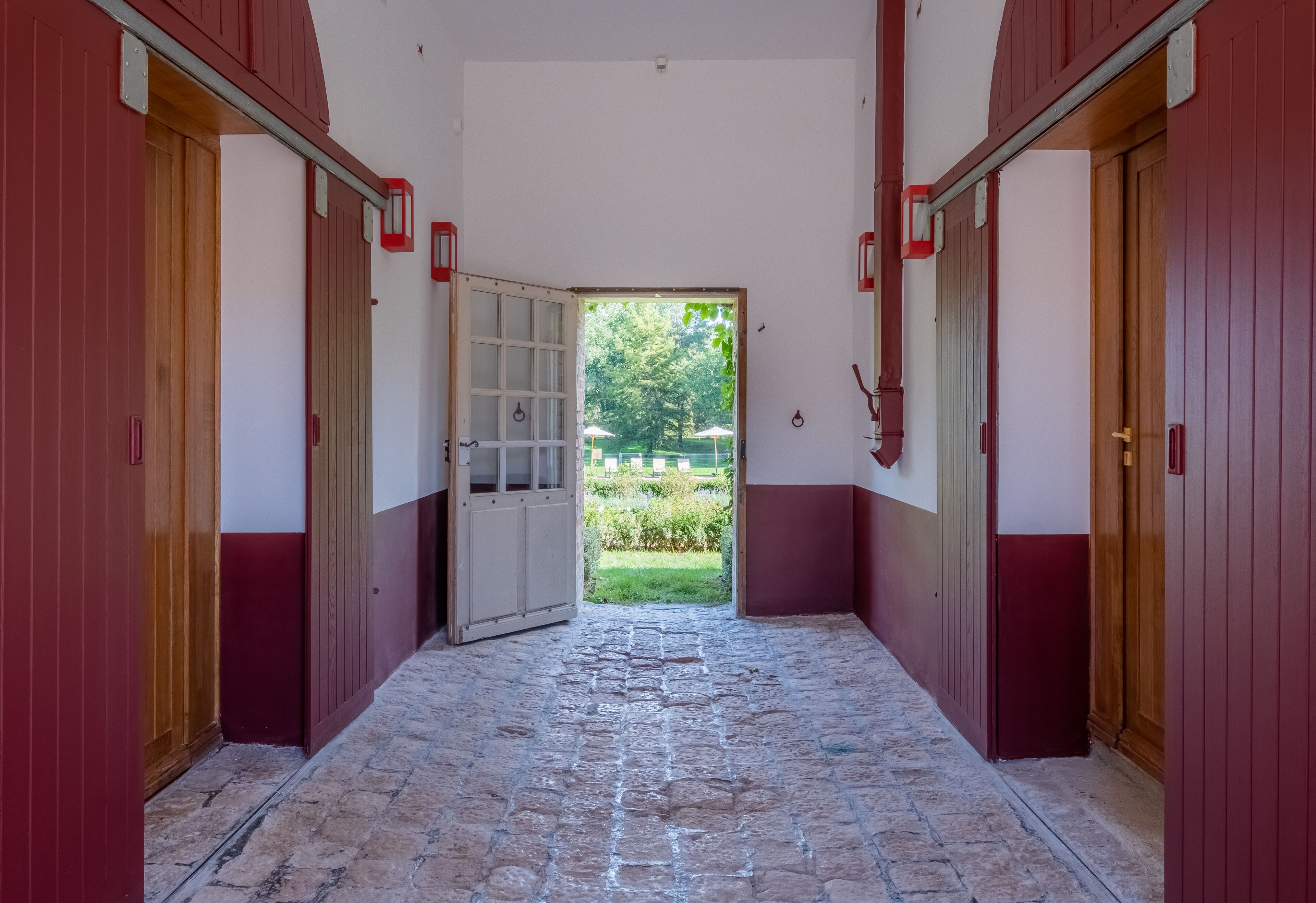 A corridor with red doors leading to a garden.