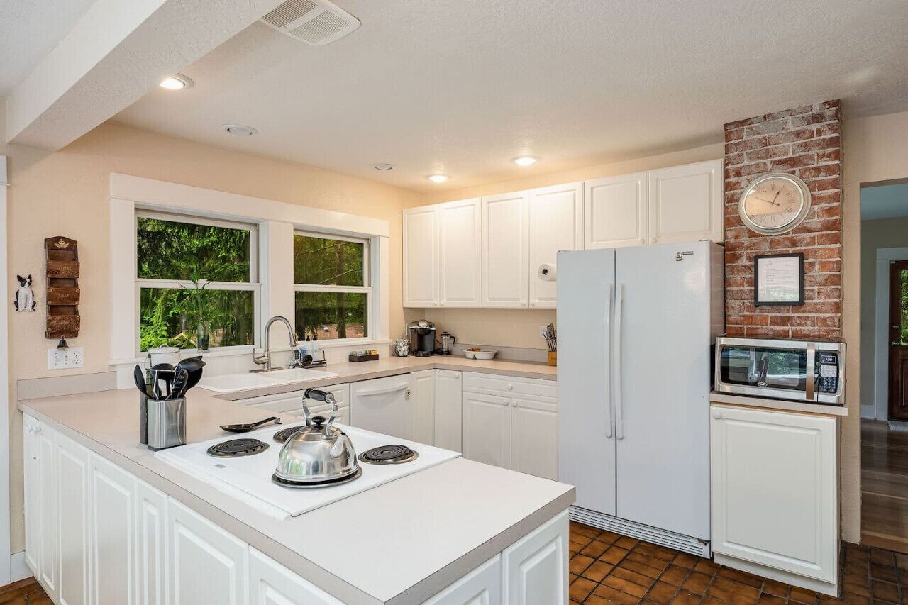 Una cocina con muebles blancos, una isla central con tetera, refrigerador y microondas.