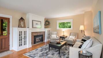 A living room with a fireplace, white cabinets, a sofa, a coffee table, and a view of greenery outside.