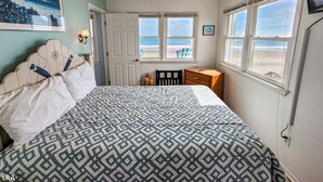 A bedroom with a bed, a ceiling fan, a nightstand, a dresser, and a window with a view of the beach. - Beach House - Pet-Friendly Oceanfront Gem (Surf City)