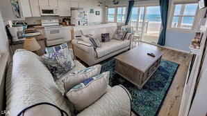 A cozy living room with a sofa, coffee table, and a view of the ocean through large windows. - Beach House - Pet-Friendly Oceanfront Gem (Surf City)