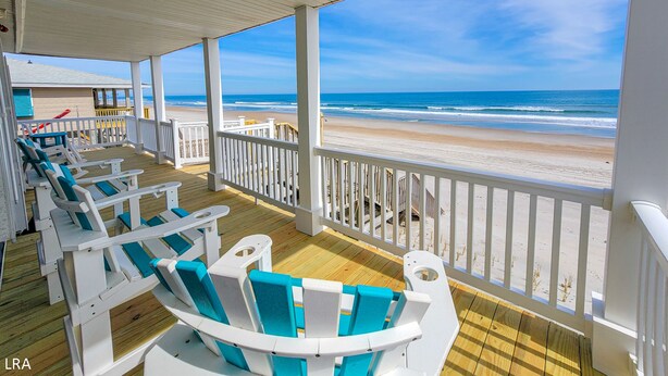 A covered deck with white and turquoise chairs, a wooden floor, and a view of the beach and ocean. - Beach House - Pet-Friendly Oceanfront Gem (Surf City)