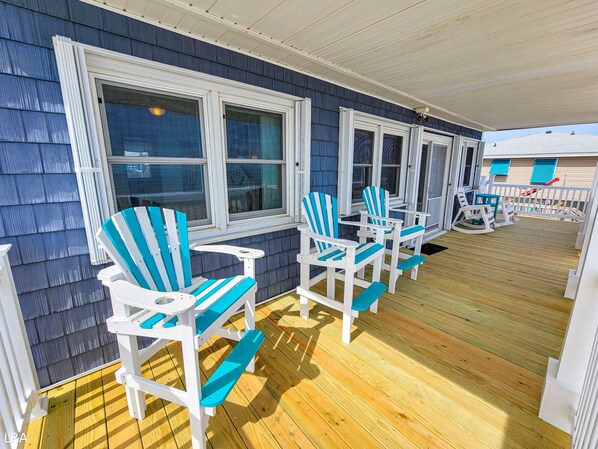 A covered deck with blue and white Adirondack chairs, wooden flooring, and a view of the house in the background. - Beach House - Pet-Friendly Oceanfront Gem (Surf City)