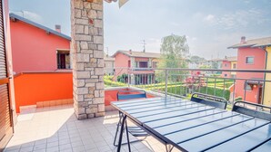 A balcony with a table and chairs, a stone pillar, and a view of neighboring houses. - Garda Orange Apartment - Italian Homing (Desenzano del Garda)