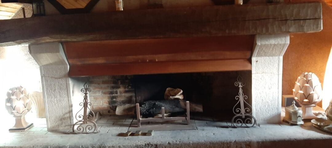 A fireplace with a stone mantle, a log fire, and decorative metal stands.