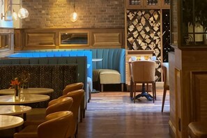 A restaurant with booths, round tables, and a brick wall. - Walker Hotel Tribeca (New York)