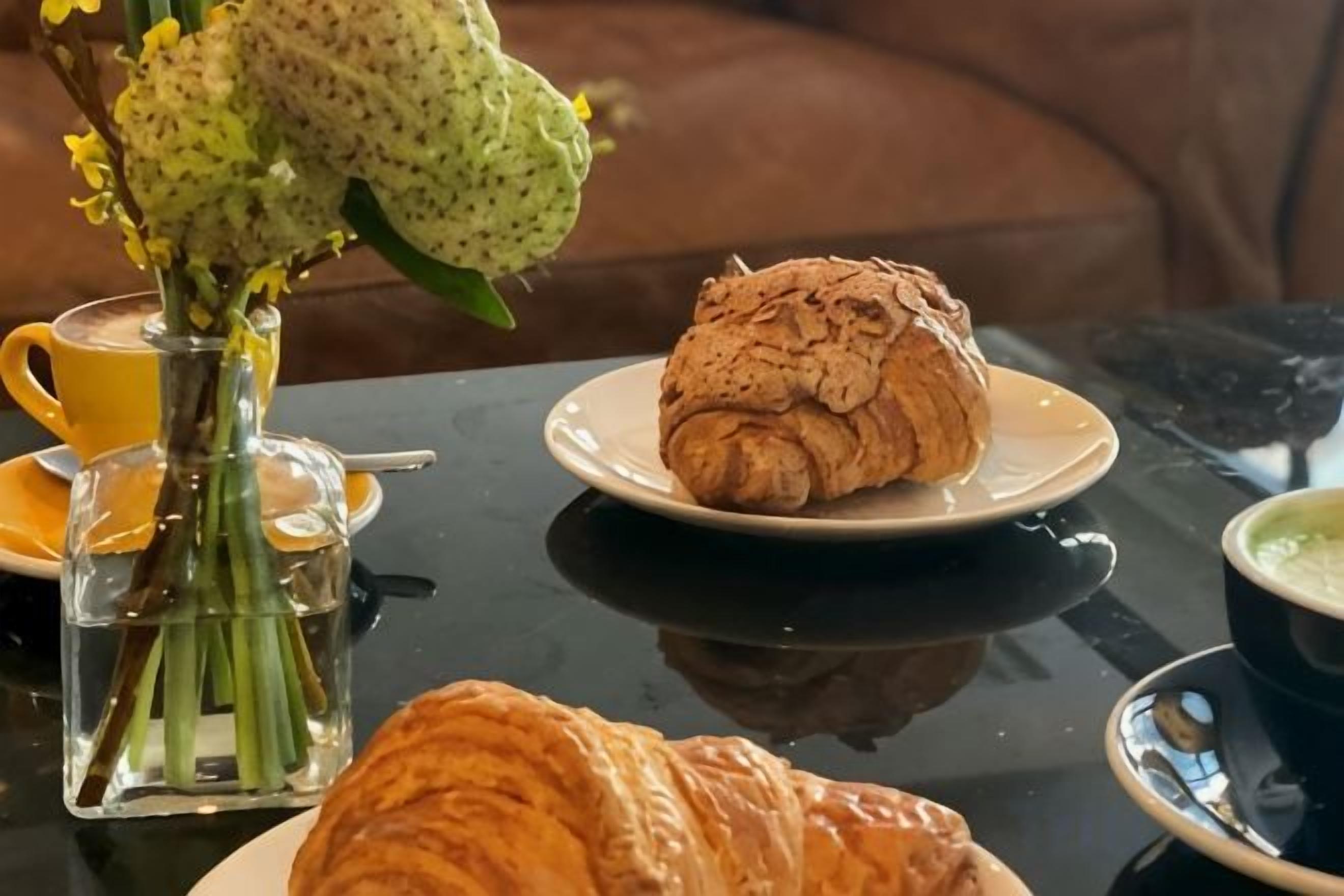 A table with a croissant, a cup of coffee, and a vase of flowers.