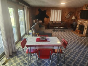 Ein Zimmer mit Esstisch, Stühlen, einer Couch, einem Kamin und einem großen Fenster.