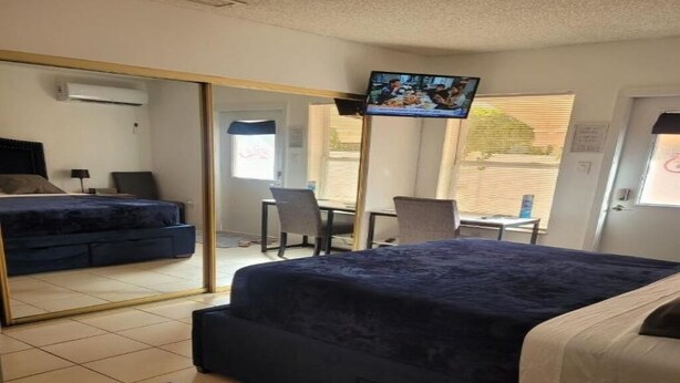 A hotel room with a bed, a desk, a chair, a TV, and a large mirror. - studio cross the street to Freedom Park Miami 3 minutes from Miami Int Airport (Miami)