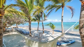 A beach with palm trees, a hammock, and a boat.