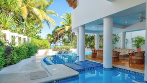 A pool area with a curved design, surrounded by palm trees and a clear view of the ocean.