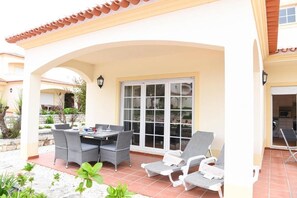 Une terrasse couverte avec une table et des chaises, une porte-fenêtre coulissante et un sol carrelé.