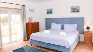 A bedroom with a bed, a dresser, a nightstand, and a view of the outside. - Casa América - Praia Del Rey (Casal da Lagoa Seca)