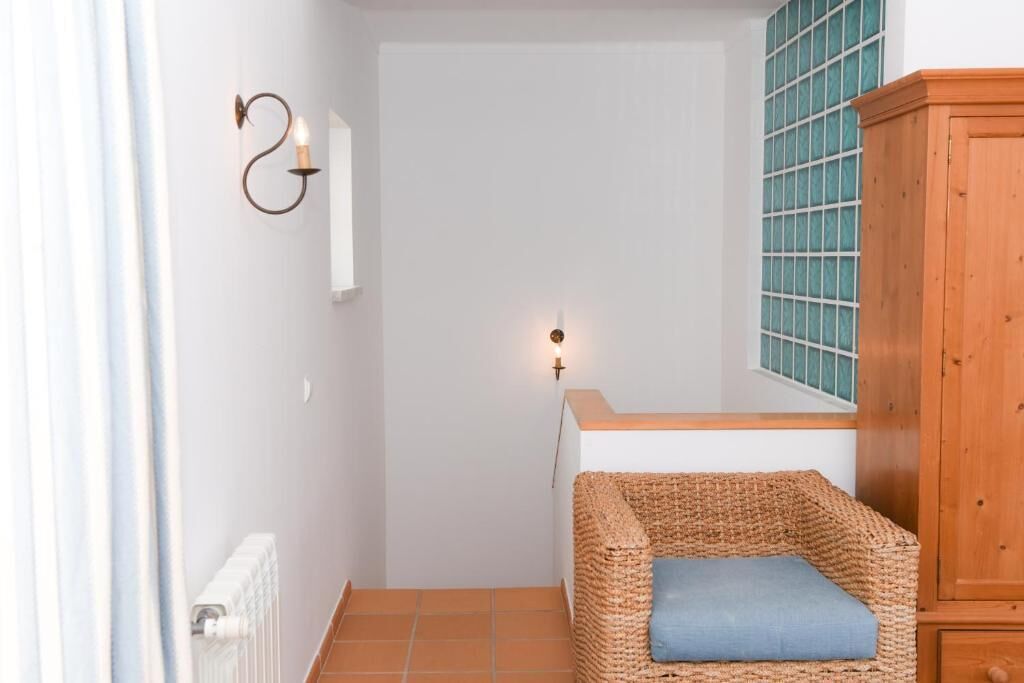 Un pasillo estrecho con una silla de mimbre, un armario de madera y una lámpara de pared.