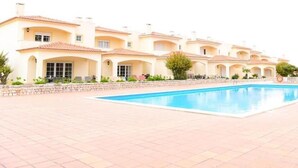 A swimming pool area with a row of buildings in the background. - Casa América - Praia Del Rey (Casal da Lagoa Seca)