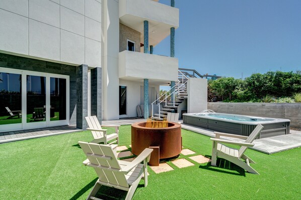 Un patio moderno al aire libre con un brasero, sillas de descanso y un jacuzzi.