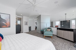 Una habitación de hotel moderna con una cama grande, un escritorio, una kitchenette y una zona de estar.