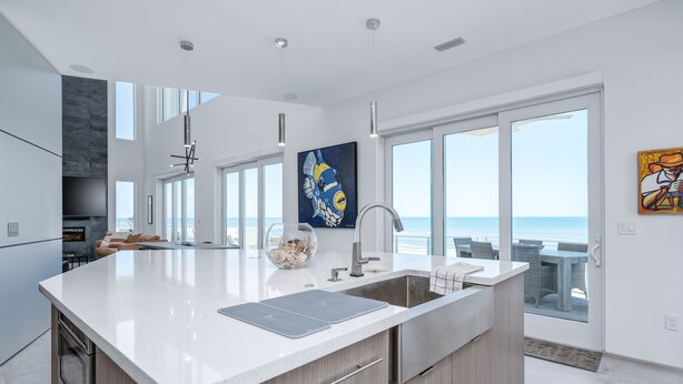 A modern kitchen with a large island, a built-in oven, and a view of the ocean through large windows.