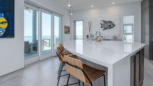 A modern kitchen with a large island, bar stools, and a view of the ocean.