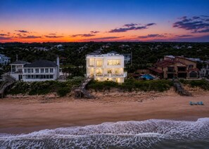 A beachfront property with a large house, a swimming pool, and a wooden staircase leading to the beach.