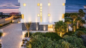 A modern building with a flat roof, rectangular windows, and a paved pathway leading to a beach.