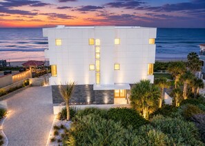 A modern building with a flat roof, rectangular windows, and a paved pathway leading to a beach.
