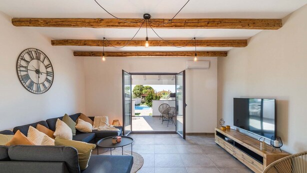 A modern living room with a sofa, TV, and a large clock on the wall.