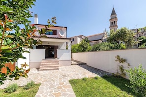 Una casa con un sendero de piedra que conduce a la entrada, rodeada de follaje y un muro blanco.
