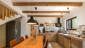 A modern kitchen with wooden beams, a central island, and a dining area with a wooden table and chairs.