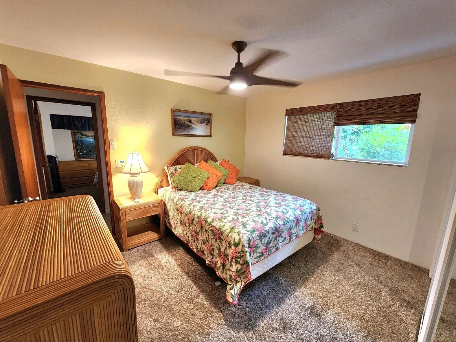 A bedroom with a bed, a nightstand, a lamp, a ceiling fan, a window with a view, and a door.