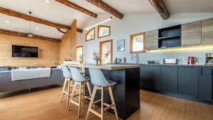A modern kitchen with a central island, bar stools, wooden beams, and a built-in TV.