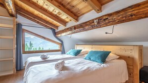 A bedroom with two beds, wooden ceiling beams, a large window with a mountain view, and a wooden headboard.