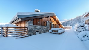 A snow-covered lodge with stone walls and wooden beams, featuring a stone entrance and a wooden deck.
