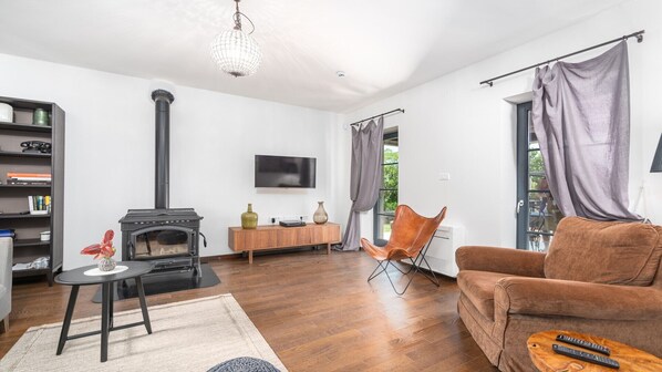 Una sala de estar moderna con una estufa de leña, un televisor de pantalla plana, un sillón de cuero y un sofá marrón.