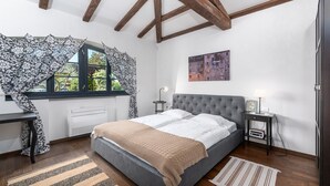 A bedroom with a bed, a window with patterned curtains, a bedside table with a lamp, and a painting on the wall. - Rustic Villa Noce with pool (Sveti Ivan)