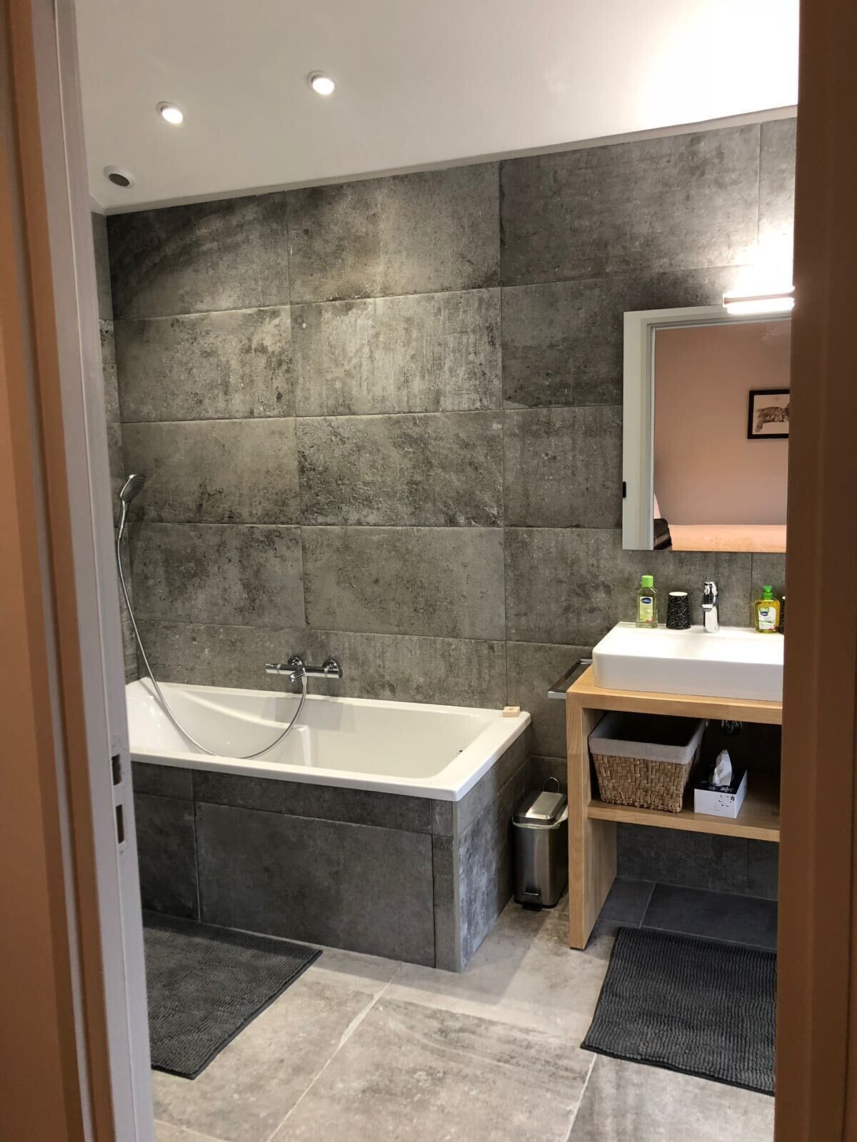 Une salle de bain moderne avec une baignoire sur pieds, un meuble-lavabo avec un miroir et une petite étagère contenant des articles de toilette.