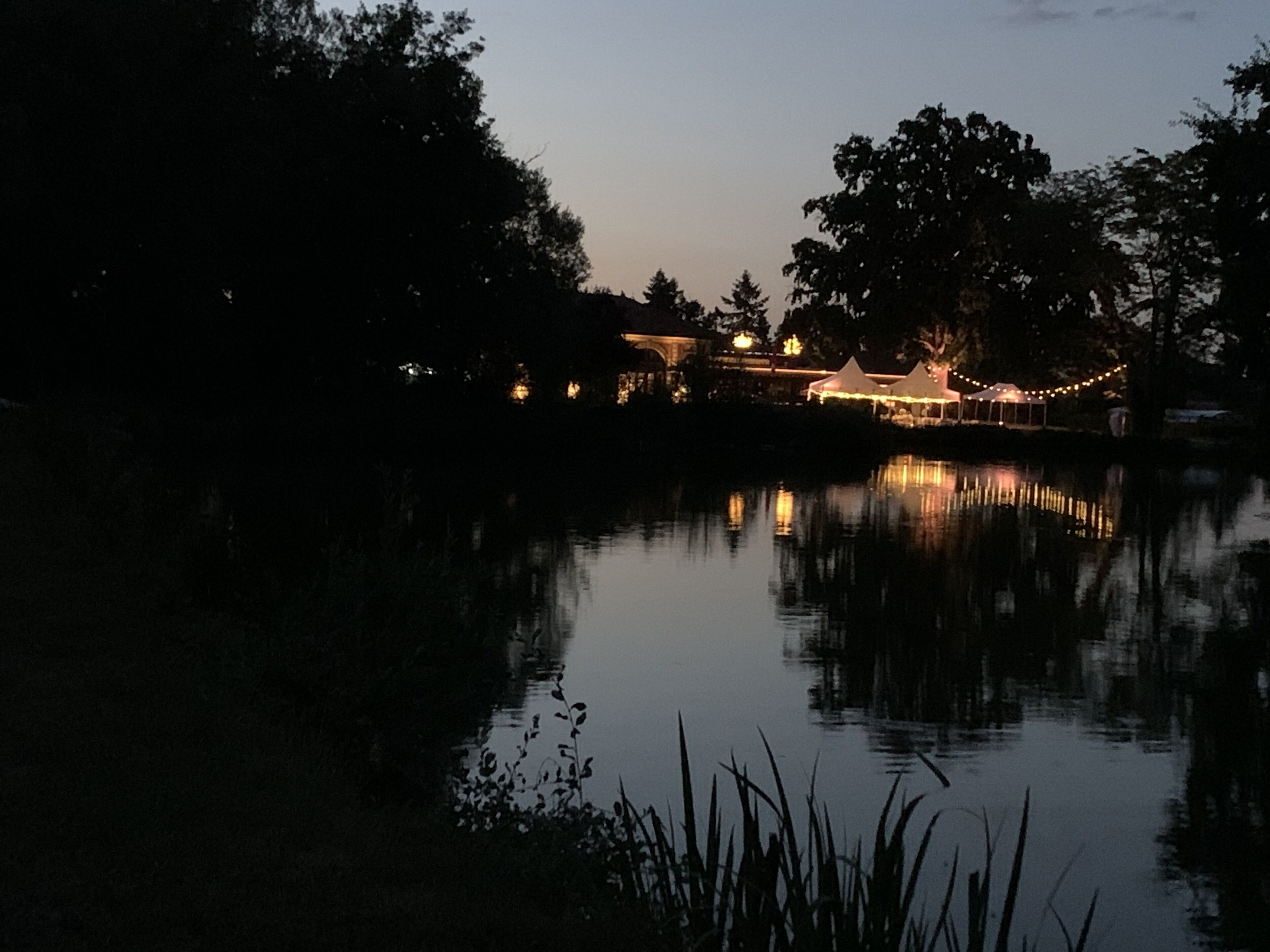 Een nachtzicht van een oever met een gebouw en tenten, verlicht door lichtslingers.