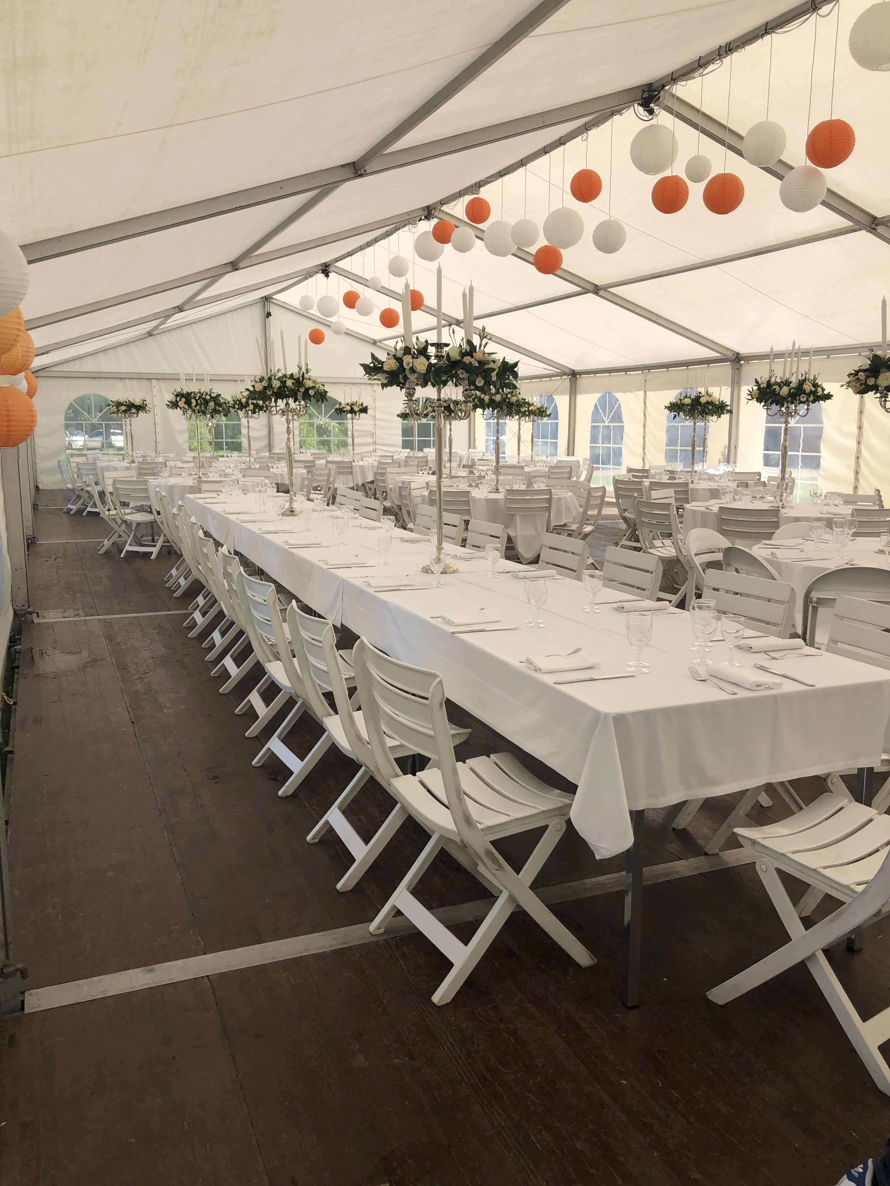 A tented event space with tables set for dining, white chairs, and floral centerpieces.