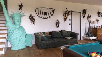 A living room with a sofa, a pool table, and a statue of the Statue of Liberty.