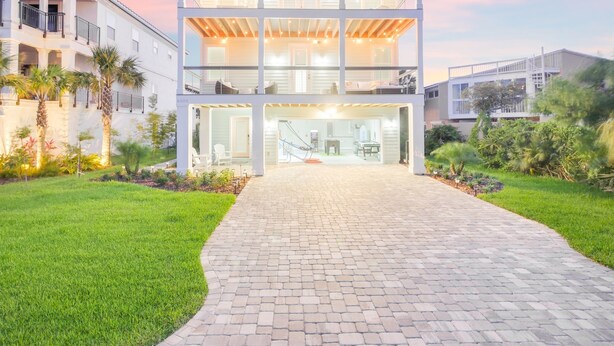 A modern two-story building with a glass facade, a paved entrance, and a landscaped garden with palm trees. - Heated Pool | Game Room | Elevator | Tiki Hut (St. Augustine)