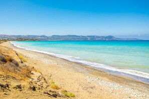 A beach with clear turquoise water, a sandy shore, and distant hills.