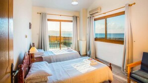 Habitación de hotel con dos camas, un balcón con vista al mar y un aire acondicionado.