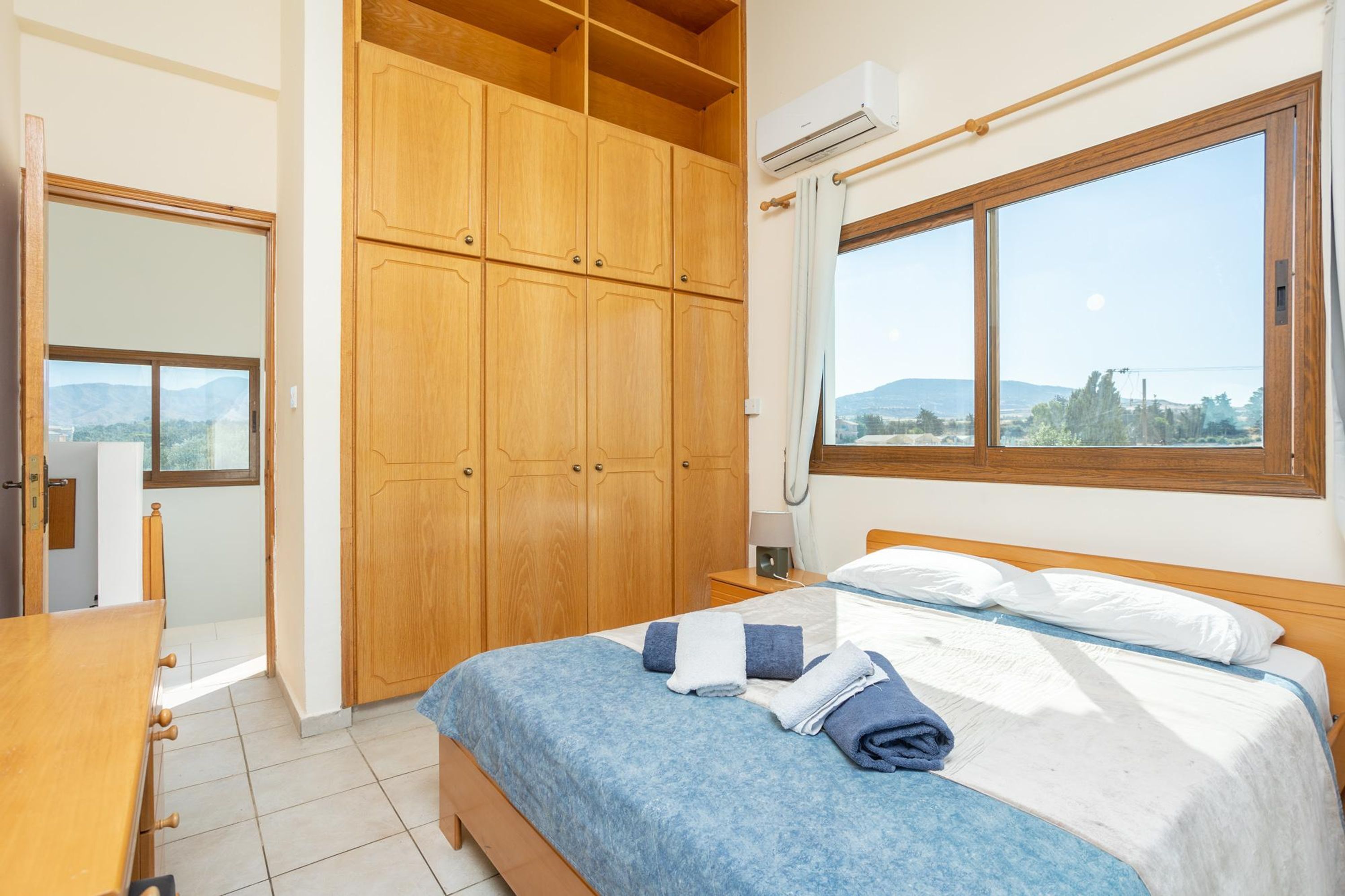 A bedroom with a bed, wooden wardrobe, and a window with a view.