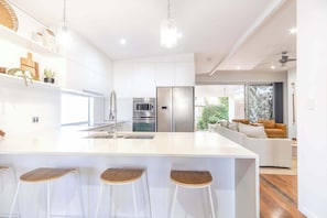 Une cuisine moderne avec des meubles blancs, un îlot central doté de tabourets, des appareils en acier inoxydable et un coin repas comprenant un canapé et une table basse.