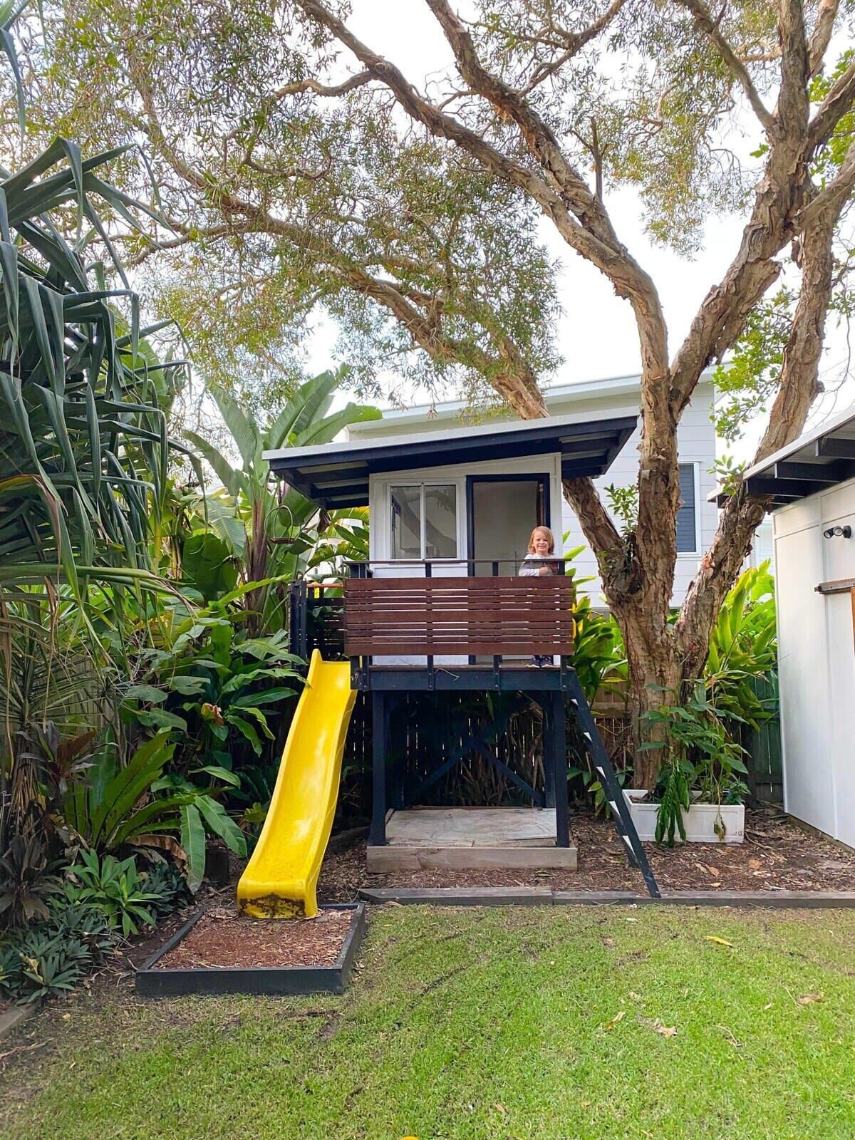 A residential backyard with a slide, a wooden deck, and a house.