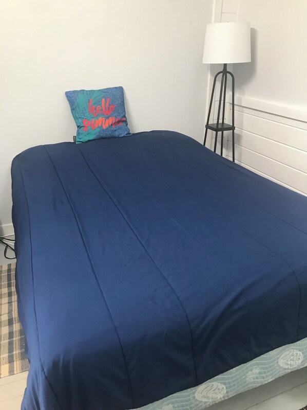 Una cama con colcha azul y almohada con texto rojo.